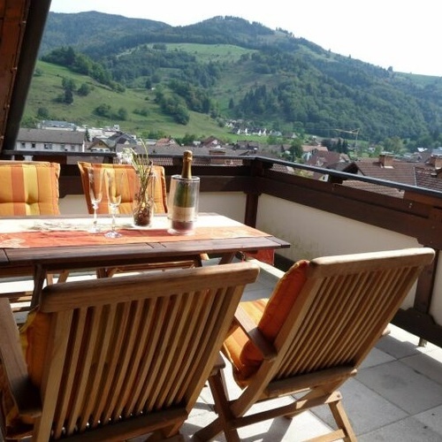 Balkon mit Holztisch und vier Stühlen im Hintergrund der Blick auf die grünen Wälder und Wiesen - Balkon mit Holztisch und vier Stühlen im Hintergrund der Blick auf die grünen Wälder und Wiesen -