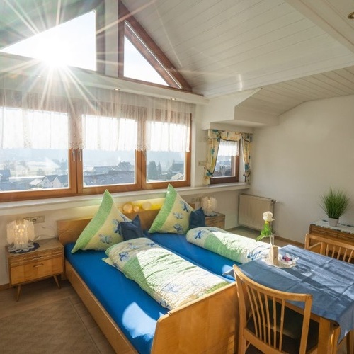 Doppelbett mit großer Fensterfront im Hintergrund und kleinem Tisch - 