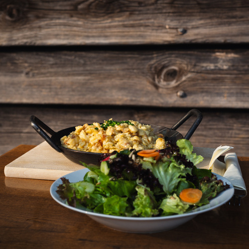 Salatteller und eine Servierpfanne mit Käseknöpfle im Hintergrund - Salatteller und eine Servierpfanne mit Käseknöpfle im Hintergrund -